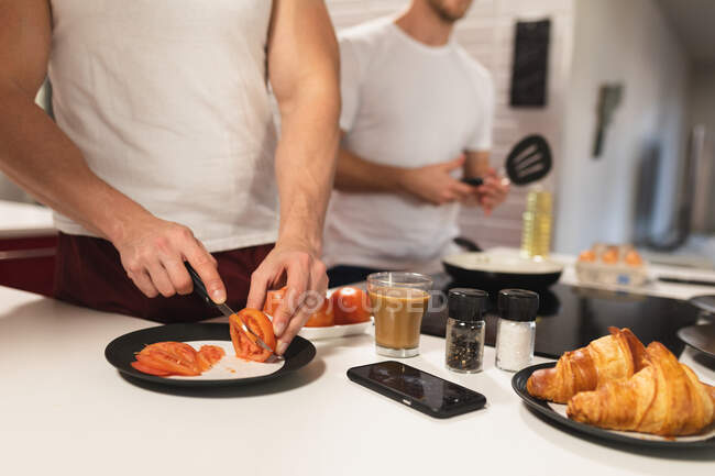 Vorderseite Mittelteil des kaukasischen männlichen Paares entspannt zu Hause, steht in der Küche und bereitet gemeinsam ein Frühstück zu — Stockfoto