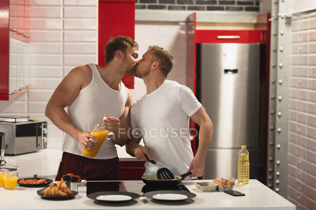 Vorderansicht eines kaukasischen männlichen Paares, das es sich zu Hause gemütlich macht, in der Küche steht, ein gemeinsames Frühstück zubereitet und sich küsst. — Stockfoto