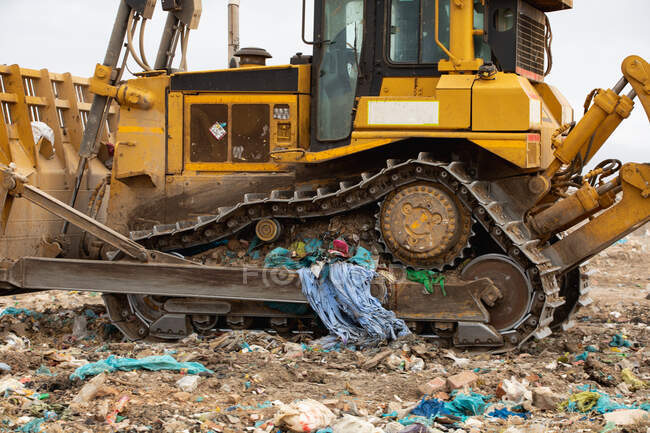 Primo piano di un bulldozer che lavora e ripulisce i rifiuti accumulati su una discarica piena di rifiuti con cielo nuvoloso coperto sullo sfondo. Questione ambientale globale dello smaltimento dei rifiuti. — Foto stock