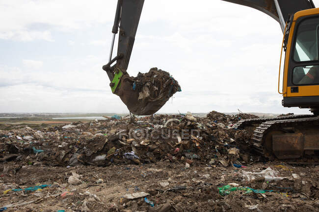 Excavadora trabajando y limpiando basura apilada en un vertedero lleno de basura con el cielo nublado nublado en el fondo. Cuestión medioambiental mundial de la eliminación de residuos. - foto de stock