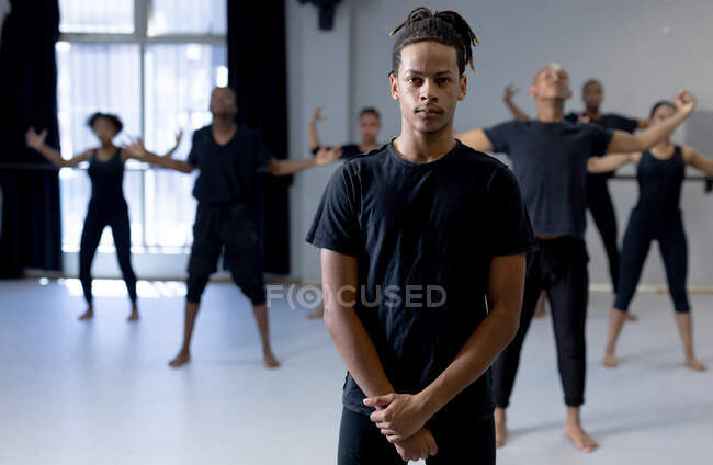 Вид спереди на танцующего мужчину смешанной расы в черной одежде, стоящего перед многоэтничной группой танцующих мужчин и женщин, смотрящих прямо в камеру. — стоковое фото