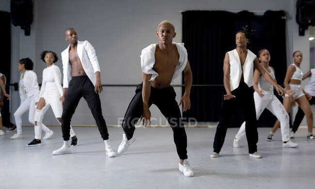 Frontansicht einer multiethnischen Gruppe fitter männlicher und weiblicher moderner Tänzer in weißen Outfits, die während eines Tanzkurses in einem hellen Studio eine Tanzroutine praktizieren. — Stockfoto