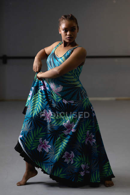 Портрет танцовщицы смешанной расы в синем цветочном платье, держащей складку и смотрящей прямо в камеру. — стоковое фото