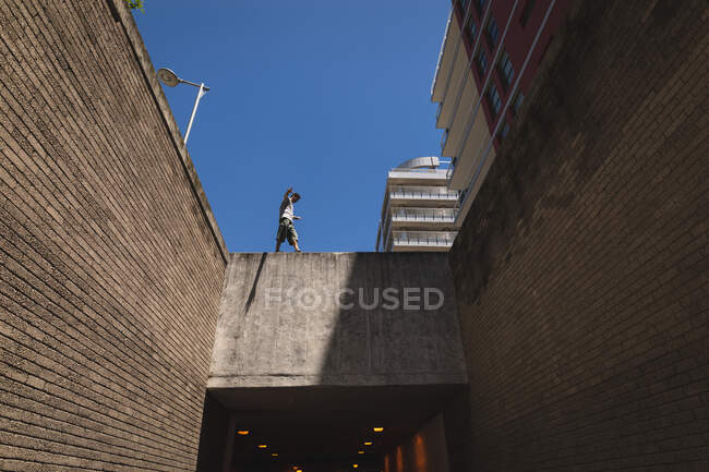 Vista frontal de un hombre caucásico practicando parkour junto al edificio en una ciudad en un día soleado, - foto de stock