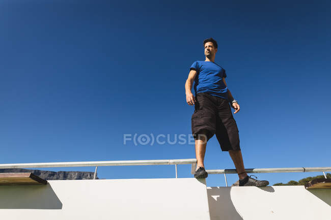 Vista frontal de um homem caucasiano praticando parkour perto do edifício em uma cidade em um dia ensolarado — Fotografia de Stock