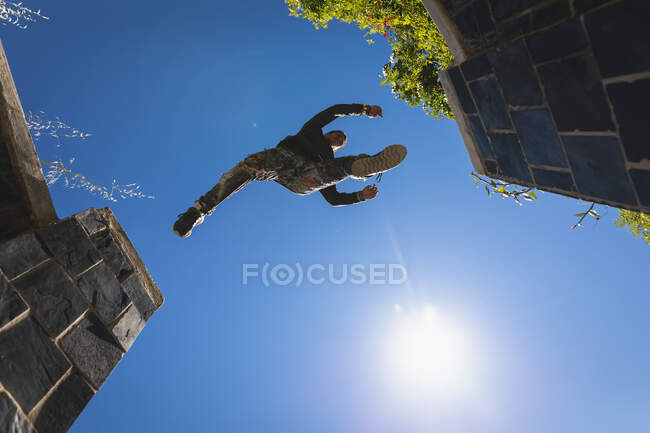 Передній низькокутний вид на кавказького чоловіка, який практикує паркур біля будинку в місті в сонячний день, стрибаючи на сходах з поручнями.. — стокове фото