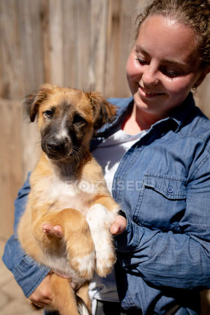 Frontansicht einer freiwilligen Helferin im Tierheim, die an einem sonnigen Tag einen geretteten Welpen im Arm hält. — Stockfoto