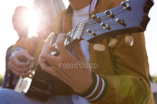 Vista laterale metà sezione da vicino di un uomo misto corsa appendere fuori su una terrazza sul tetto in una giornata di sole, suonare la chitarra — Foto stock