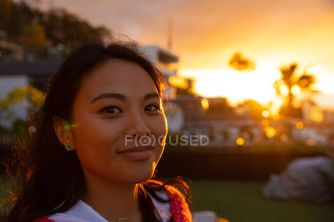 Retrato de uma mulher asiática pendurada em um terraço com um céu de pôr do sol, olhando para a câmera e sorrindo — Fotografia de Stock