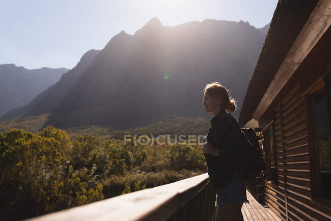 Vista laterale di una donna caucasica che si diverte in un viaggio in montagna, in piedi su un balcone cabina, godendo la sua vista, in una giornata di sole — Foto stock