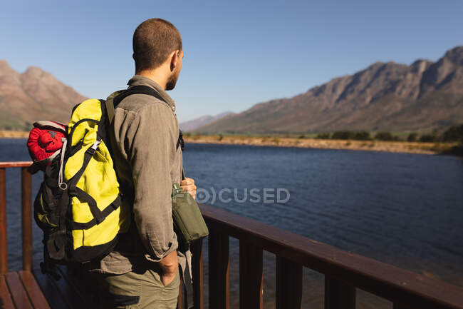 Side view of a Caucasian man having a good time on a trip to the mountains, standing on a cabin balcony, enjoying his view, on a sunny day — Stock Photo