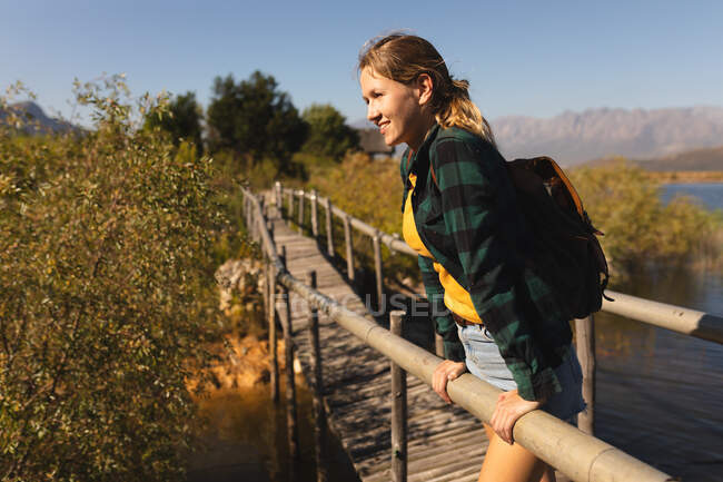 Vista lateral de uma mulher caucasiana se divertindo em uma viagem às montanhas, de pé em uma ponte, apreciando sua vista, apoiando-se em uma barreira em um dia ensolarado — Fotografia de Stock