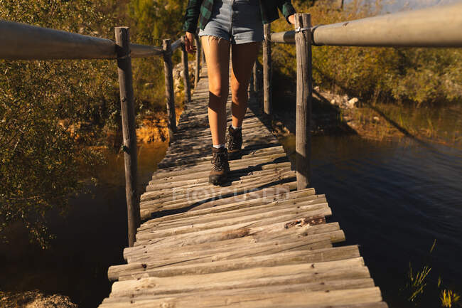 Vista frontal seção baixa de mulher se divertindo em uma viagem às montanhas, de pé em uma ponte, em um dia ensolarado — Fotografia de Stock