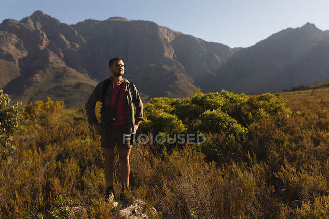 Вид спереди кавказца, хорошо проводящего время в поездке в горы, стоящего на скале, в солнечный день — стоковое фото