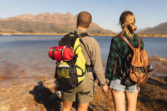 Vista posteriore da vicino di una coppia caucasica che si diverte durante una gita in montagna, in piedi su una riva, tenendosi per mano, in una giornata di sole — Foto stock