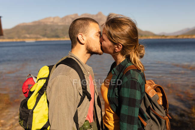 Seitliche Nahaufnahme eines kaukasischen Paares, das sich bei einem Ausflug in die Berge amüsiert, am Ufer steht, sich küsst, an einem sonnigen Tag — Stockfoto