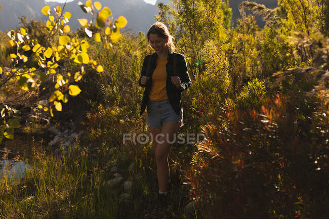 Vista frontale di una donna caucasica che si diverte durante una gita in montagna, camminando su un campo, in una giornata di sole — Foto stock
