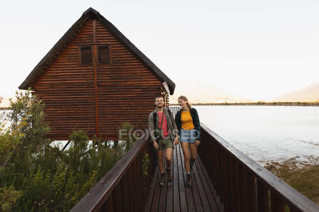 Vista frontal de um casal caucasiano se divertindo em uma viagem às montanhas, andando em uma ponte em direção à câmera, de mãos dadas — Fotografia de Stock