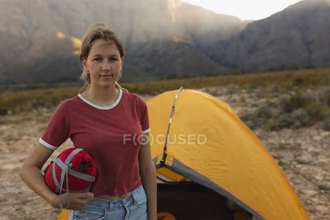Portrait of a Caucasian woman having a good time on a trip to the mountains, looking at the camera, standing by a tent — Stock Photo