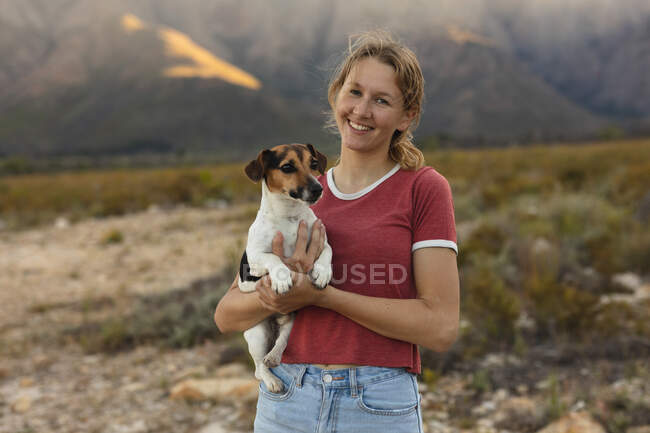 Ritratto di una donna caucasica che si diverte durante un viaggio in montagna, guarda la macchina fotografica, tiene in braccio un cucciolo, sorride — Foto stock