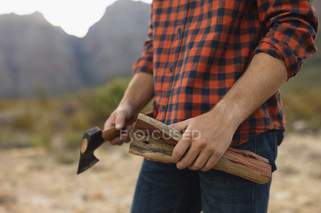 Side view mid section close up of man having a good time on a trip to the mountains, holding a log and an axe — Stock Photo