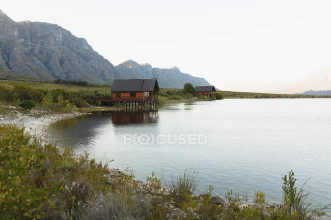 Atemberaubender Blick auf eine einsame Holzhütte, die an einem bewölkten Tag am Ufer eines Sees in der Nähe der Berge steht — Stockfoto