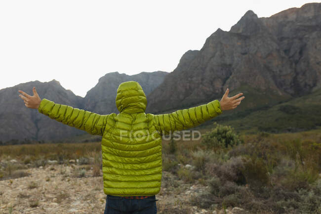 Передній вид на кавказького чоловіка, який добре проводить час, подорожуючи горами, одягаючи теплий одяг, насолоджуючись своїм поглядом, тримаючи руки широко. — стокове фото