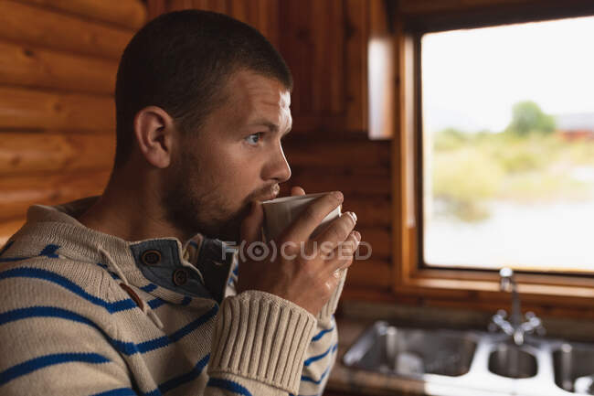 Seitliche Nahaufnahme eines kaukasischen Mannes, der eine gute Zeit auf einer Reise in die Berge hat, in einer Holzhütte sitzt und Kaffee trinkt — Stockfoto