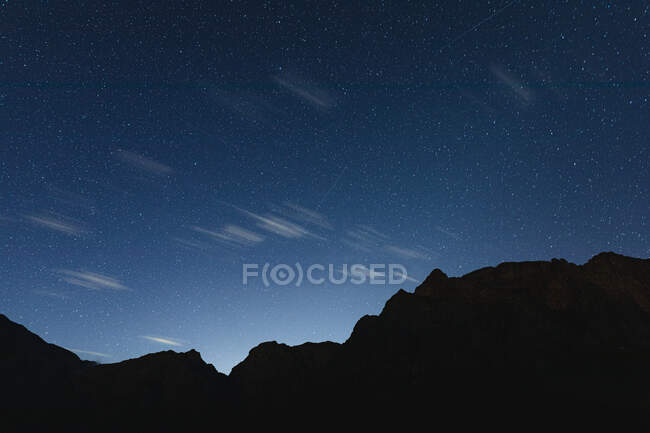 Atemberaubender Blick auf einen Nachthimmel über Bergen mit Hunderten von Sternen und einigen schwebenden Wolken, die Sonne beginnt aufzugehen — Stockfoto