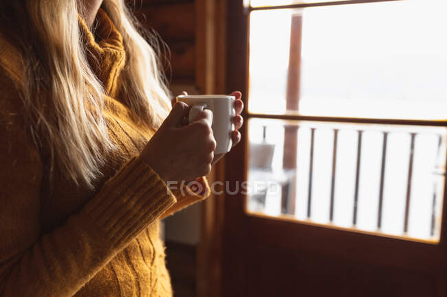 Vista lateral mid section close up de mulher tendo um bom tempo em uma viagem para as montanhas, sentado em uma cabine de madeira, beber café, segurando uma xícara — Fotografia de Stock