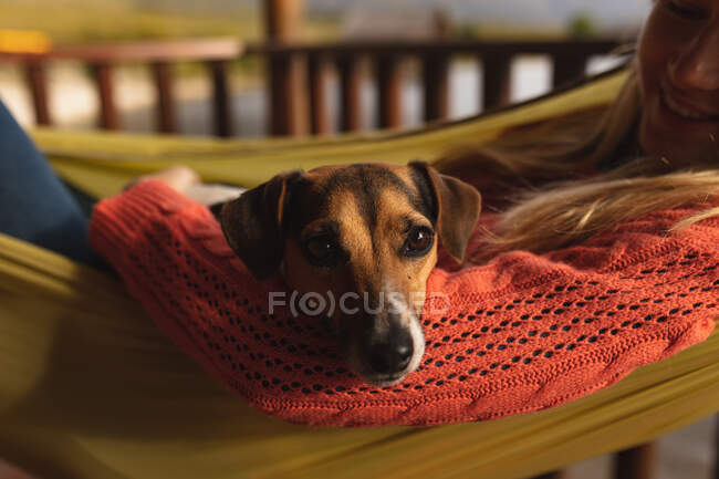 Vista lateral de perto de uma mulher caucasiana se divertindo em uma viagem às montanhas, deitada em uma rede, com um filhote de cachorro na barriga — Fotografia de Stock