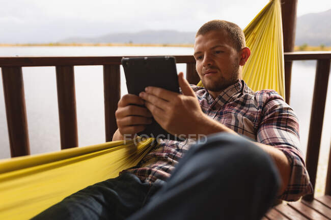 Vorderseite Nahaufnahme eines kaukasischen Mannes, der eine gute Zeit auf einer Reise in die Berge hat, auf einer Hängematte liegend, mit einem digitalen Tablet — Stockfoto