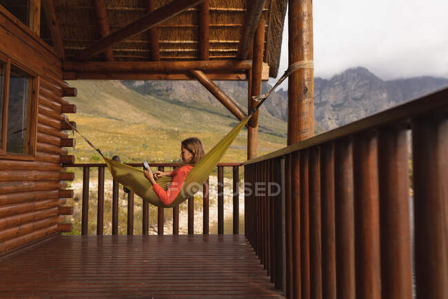 Вид сбоку на кавказку, хорошо проводящую время в поездке в горы, лежащую на гамаке, с помощью цифровой планшета — стоковое фото