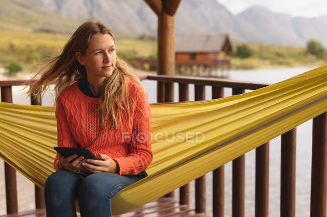 Front view of a Caucasian woman having a good time on a trip to the mountains, sitting on a hammock, using a digital tablet — Stock Photo