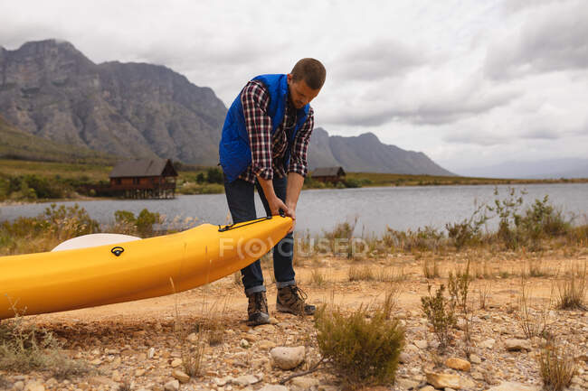 Vista frontal de cerca de un hombre caucásico pasándola bien en un viaje a las montañas, preparando un kayak - foto de stock