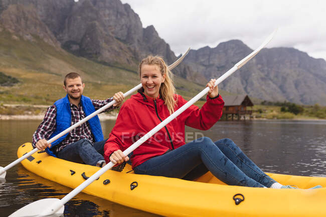 Vista frontal de una pareja caucásica pasando un buen rato en un viaje a las montañas, kayak en un lago, sonriendo - foto de stock
