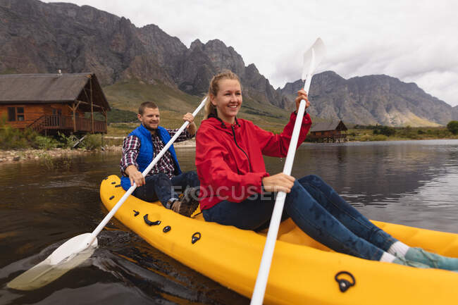 Vista frontal de una pareja caucásica pasando un buen rato en un viaje a las montañas, kayak en un lago, sonriendo - foto de stock