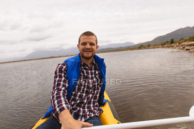 Передній вид кавказького чоловіка добре проводить час у подорожі в гори, катаючись на озері, дивлячись на камеру, усміхаючись — стокове фото