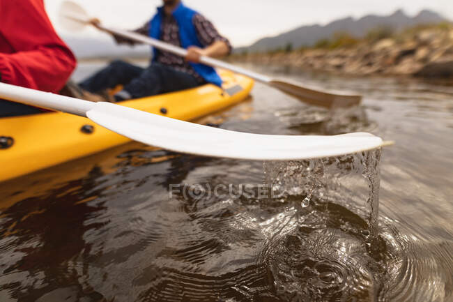 Side view close up of couple having a good time on a trip to the mountains, kayaking on a lake, pulling the ores from the water — Stock Photo