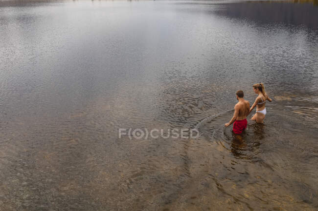 Vista lateral de alto ângulo de um casal caucasiano se divertindo em uma viagem às montanhas, caminhando até o lago, de mãos dadas — Fotografia de Stock