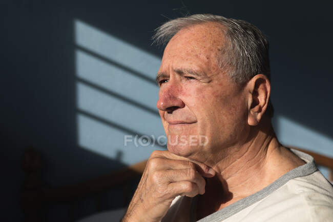 Seitliche Nahaufnahme eines älteren kaukasischen Mannes, der es sich zu Hause in seinem Schlafzimmer gemütlich macht, in der Sonne sitzt und nachdenkt, nachdem er am Morgen aufgestanden ist — Stockfoto