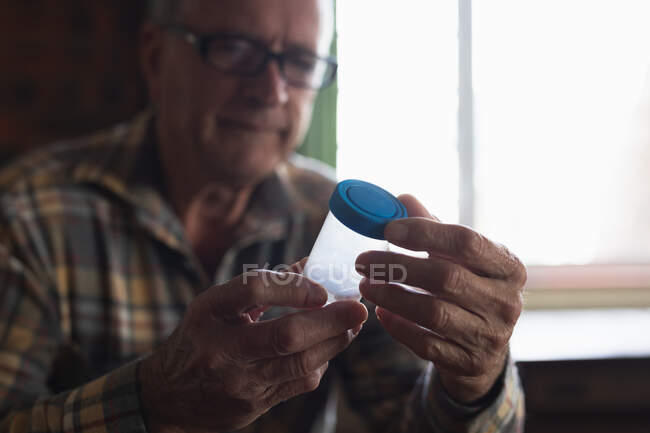Vorderseite Nahaufnahme eines älteren kaukasischen Mannes, der zu Hause sitzt und eine Tablettenschachtel mit Medikamenten hält, Fokus auf den Vordergrund — Stockfoto