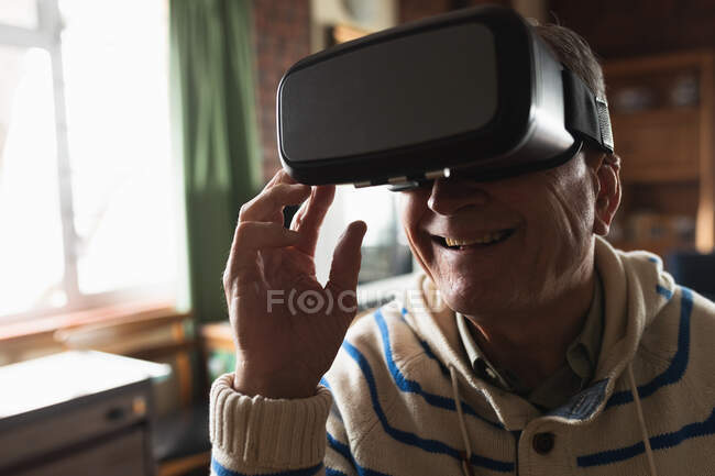 Вид сбоку крупным планом старшего кавказца, расслабляющегося дома в своей гостиной, сидящего за столом, используя гарнитуру виртуальной реальности — стоковое фото