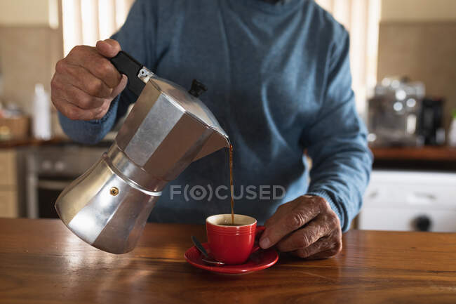 Vista frontal sección media del hombre relajándose en casa, vertiendo café fresco de una cafetera en su taza - foto de stock