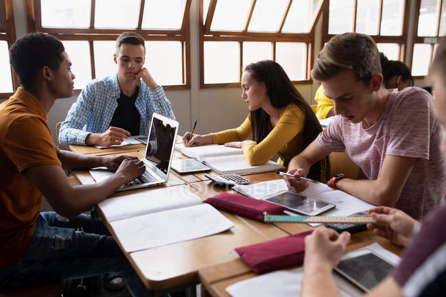 Вид збоку на багатоетнічну групу учнів середньої школи-підлітків у класі, які разом сидять за столом — стокове фото