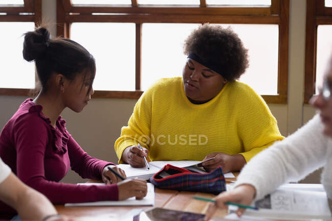 Vista frontale di due studentesse afroamericane adolescenti in classe, sedute a un tavolo a lavorare insieme e parlare — Foto stock