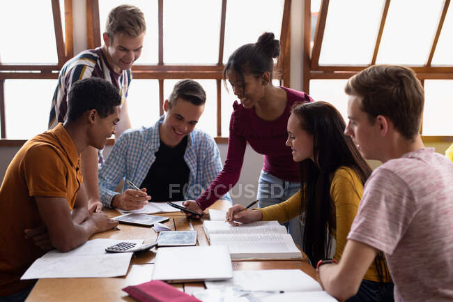 Vista laterale di un gruppo multietnico di alunni delle scuole superiori adolescenti di sesso maschile e femminile in classe, seduti a un tavolo a lavorare insieme, parlare e sorridere — Foto stock