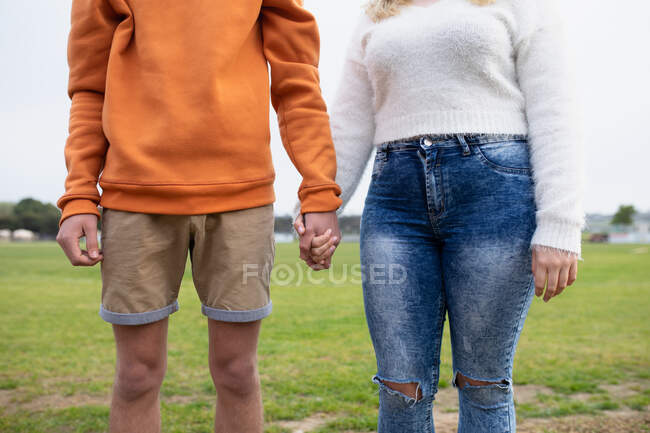 Вид спереди на среднюю часть пары старшеклассниц и школьниц, тусующихся и держащихся за руки, стоя на школьном игровом поле — стоковое фото