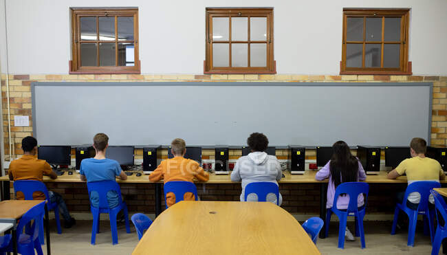 Visão traseira de um grupo multi-étnico de adolescentes alunos do ensino médio do sexo masculino e feminino em uma sala de aula, trabalhando em computadores e concentrando — Fotografia de Stock