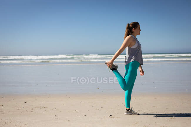 Вид сбоку на кавказскую привлекательную женщину с длинными волосами, в спортивной одежде, практикующую йогу, растянувшуюся в позиции йоги, на солнечном пляже. — стоковое фото